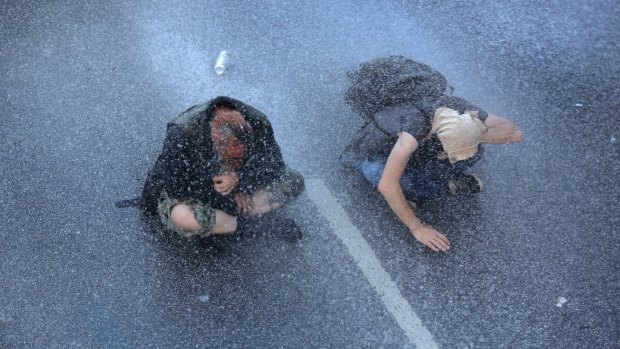 Two protesters sit on a street while the police use a water canon in Hamburg, northern Germany, on Thursday.