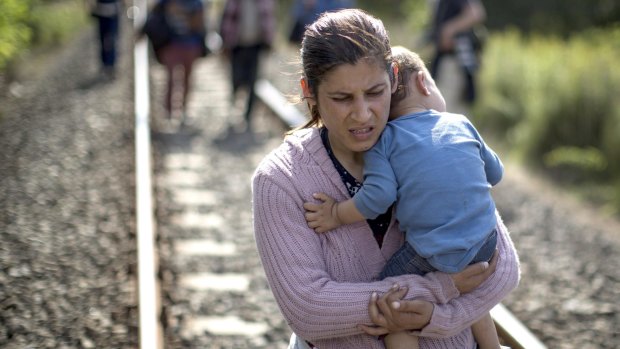 A woman carries a child as she walks along rail tracks close to the Serbian border in Hungary.