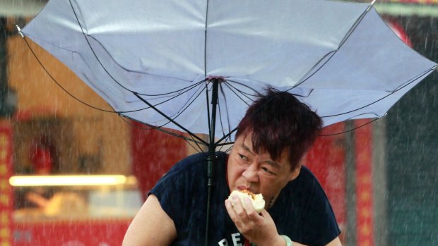 A woman, Mrs Dai, eats a pork bun while struggling with her umbrella against the powerful generated by typhoon Megi in Taipei in a photo that went viral this week.