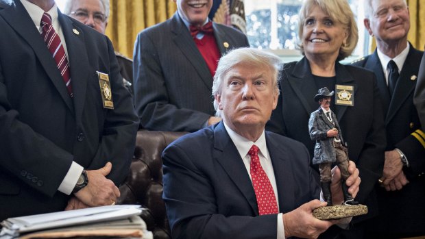 US President Donald Trump holds up a statue he received as a gift while meeting with county sheriffs in the Oval Office on Tuesday.