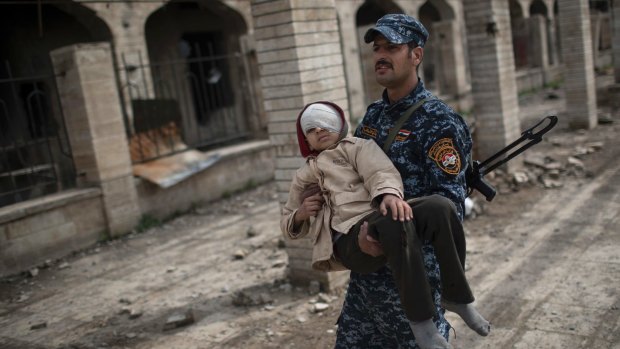 A federal police officer carries an injured boy through a destroyed train station during fighting between Iraqi security forces and Islamic State militants on the western side of Mosul.