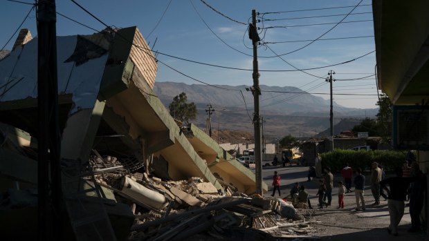 People walk next to a destroyed house after an earthquake in the city of Darbandikhan, northern Iraq, on Monday.