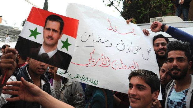 Pro-government protesters hold a portrait of President Basharal- Assad and a placard that reads, "Down with everyone who cooperated and supported the American aggression" in Damascus on Tuesday.