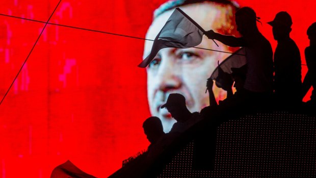 People wave Turkish flags in front of an electronic billboard displaying the face of President Recep Tayyip Erdogan after the coup attempt.