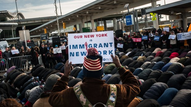 A group of Muslim men pray while supporters hold up signs during an interfaith prayer and rally against the ban at John F. Kennedy Airport.