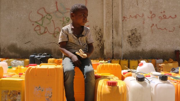 A Yemeni boy waits in line for water in Taiz. He begs for food and is eating bread he got from a nearby bakery.  