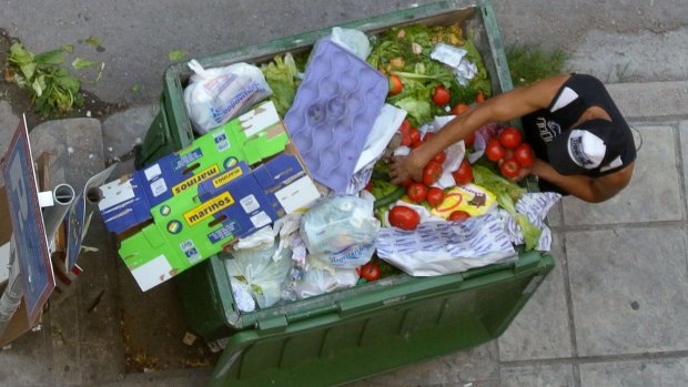 A man collects tomatoes from a garbage been outside a supermarket in Thessaloniki, Greece.