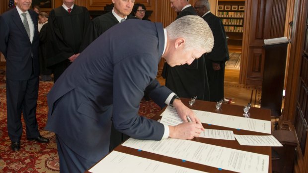 Neil Gorsuch signs the Constitutional Oath in the Justices' Conference Room at the Supreme Court in Washington as fellow justices watch on.