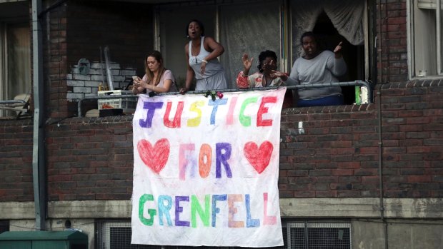 People watch from a balcony as people walk during a demonstration following the fire at Grenfell Towers.
