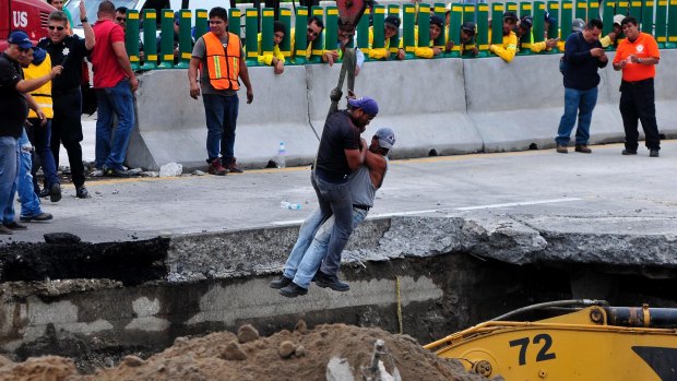 Workers are lowered by a crane as they work to rescue a vehicle that drove into a sinkhole on a highway in Cuernavaca, Mexico. 