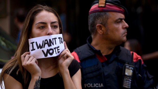A pro-independence demonstrator cover her mouth with a banner next to a Catalan police officer in Barcelona, Spain.