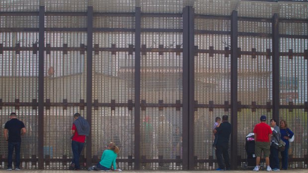 Family on the US side of the border, visit with their family members in Mexico through the border fence.