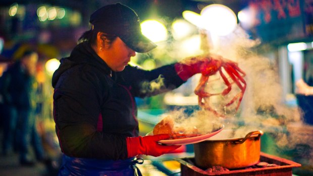 A vendor prepares freshly steamed crab at an outdoor market in South Korea.