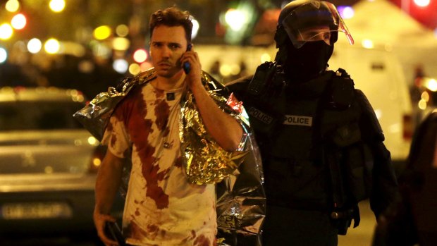 A French policeman assists a blood-covered victim near the La Bataclan concert hall.