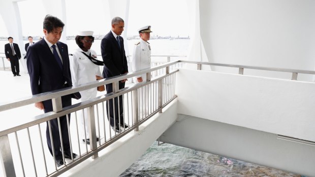 Barack Obama and Shinzo Abe pause after participating in a wreath laying ceremony overlooking the wreckage of the sunken ship where more than 1000 US service members are entombed.