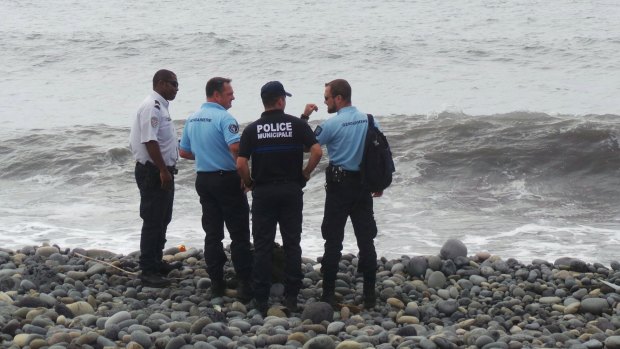 French gendarmes and police stand on the beach where a large piece of plane debris was found.