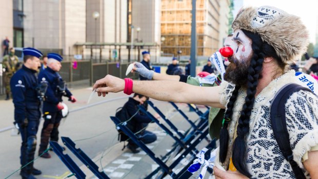 A demonstrator dressed as a clown attempts to hand a message to police during a protest outside  the European Council building in Brussels during the signing. 