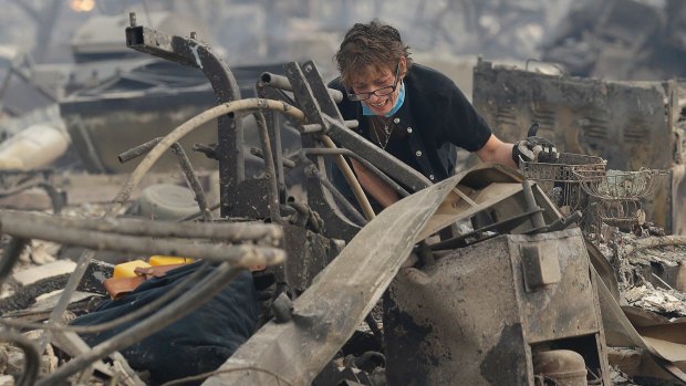 A woman reacts as she searches the remains of her family's home destroyed by fires in California.