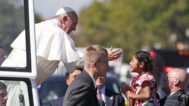 Pope Francis reaches from the popemobile for a child that is brought to him, during a parade in Washington.