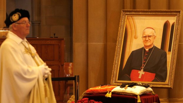 A priest stands close to a portrait of Cardinal Edward Clancy.