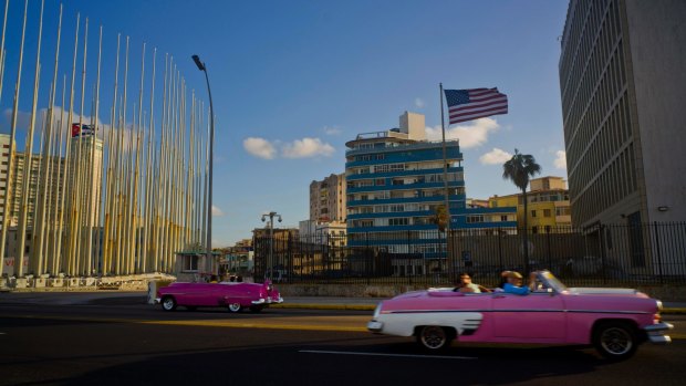 Tourists ride in classic American convertible cars past the United States embassy, right, in Havana, Cuba. The US has recalled diplomats after a spate of unexplained "sonic attacks".