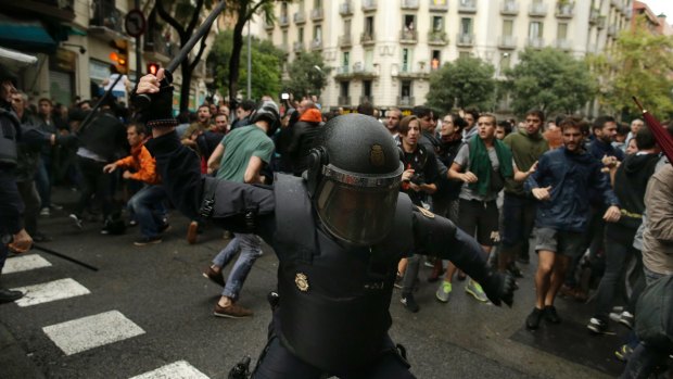 A Spanish riot police officer swings a club at would-be voters in Barcelona.