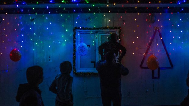 A man helps a boy to put some Christmas lights up in a camp in Erbil, where Christians displaced by Islamic State are living.