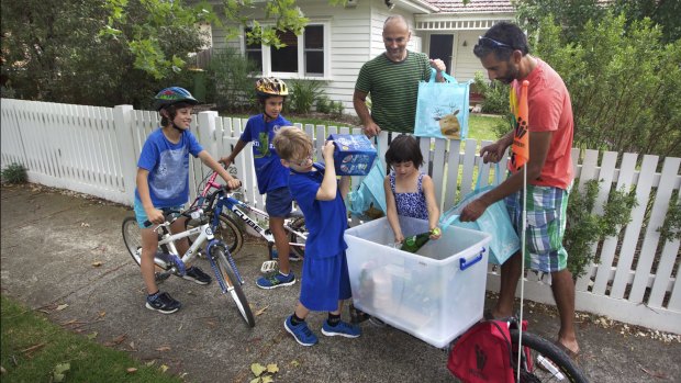 Indy Lingham (far right) and children Sage, Taj (far left) and sister Mieka load up their trailer bike with food from neighbours Milo (with package) and Angela Sansano (over fence).  
