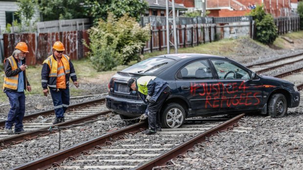 Workers prepare to tow the protesters' car from the tracks at Ascot Vale.