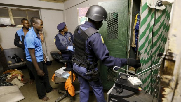 Residents watch as police search a room during a raid on a hostel in Johannesburg's Alexandra township.