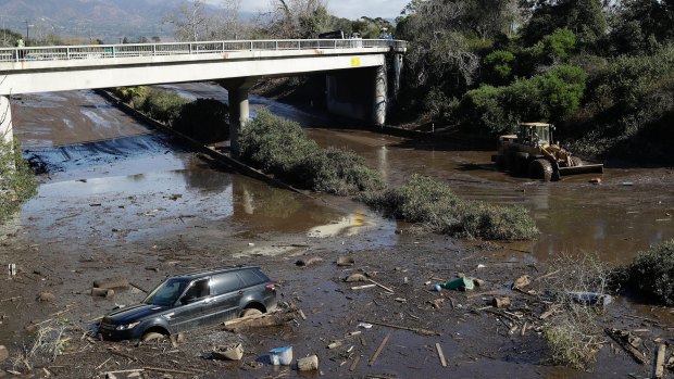 A bulldozer moves debris as a car sits stranded in a flooded section of Highway 101 in California.