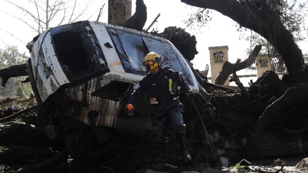 A member of the Los Angeles County Fire Department Search and Rescue crew works near a car trapped under mud and debris in Montecito.