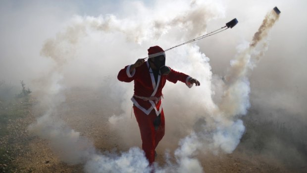 A Palestinian protester, dressed as Santa Claus, uses a slingshot to return a tear gas canister fired by Israeli troops during clashes in the occupied West Bank village of Bilin on Boxing Day.