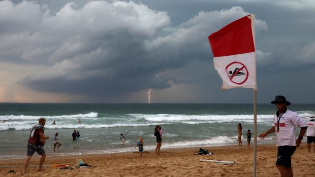 Jake Spooner a Wollongong City Council Lifeguard raises the no swim flag closing Austinmer beach as a Southerly storm moves up the coast. 