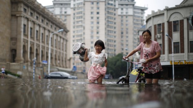A child carries kettles through a flooded street with a woman in Tianjin, China. 
