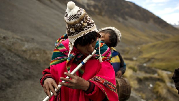 A pilgrim carries his son on his back and plays a traditional Andean flute known as a quena, as he walks to the Sanctuary of the Lord of the Qoyllur Riti, to take part in the Snow Star festival.