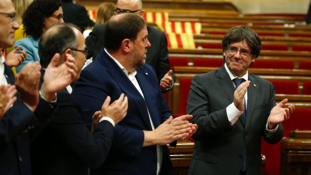 Catalonia regional President Carles Puigdemont, right, applauds with parliamentarians, after the vote to set the referendum date.