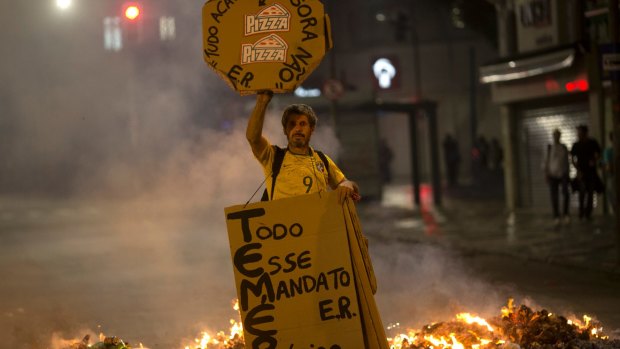 A demonstrator holds signs against Brazil's President Michel Temer at a burning road block set up by protesters in Rio de Janeiro on Thursday.