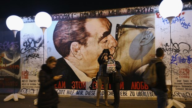 Visitors take a selfie at a mural showing former Soviet leader Leonid Brezhnev (L) kissing former East German communist leader Erich Honecker, by Russian painter Dmitri Vrubel, under a light installation illuminating the course of the Berlin Wall along an original section of the Wall called the East Side Gallery two days before the 25th anniversary of the fall in November.