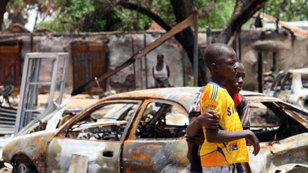 Two boys stand in front of burnt cars in Michika, a city recaptured from Boko Haram by the Nigeria military early this year.