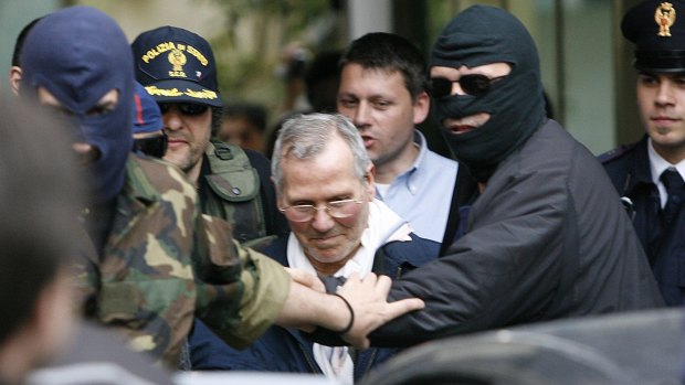 Mafia boss Bernardo Provenzano escorted by black-hooded police officer as he enters a police building in  Palermo, 2006. 