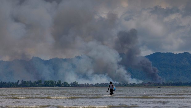 A Bangladeshi boy walks towards a parked boat as smoke rises from across the border in Myanmar, at Shah Porir Dwip, Bangladesh. 