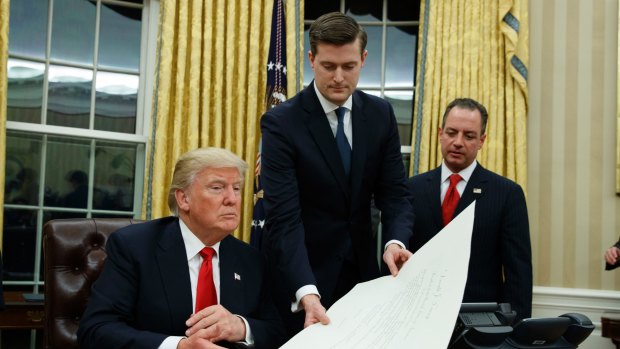 White House Chief of Staff Reince Priebus, right, watches as White House Staff Secretary Rob Porter, center, hands President Donald Trump a confirmation order for James Mattis as Defense Secretary. 