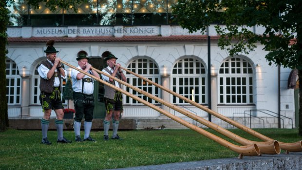 Bavarian musicians playing their Alphorns in front of the Alpsee.