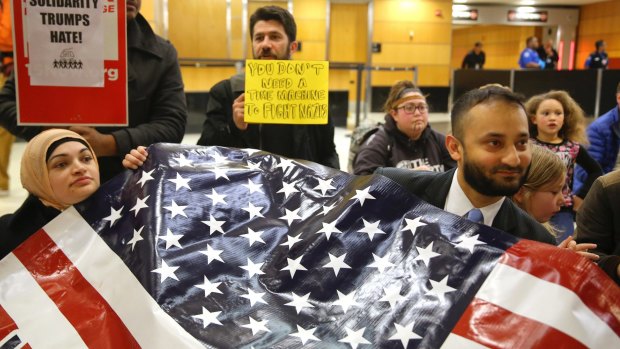 Sabrina Sheikh, left, a naturalised citizen who immigrated to the US from Pakistan at age two, and Arsalan Bukhari, right, hold up a flag that reads "We are America" in Seattle.