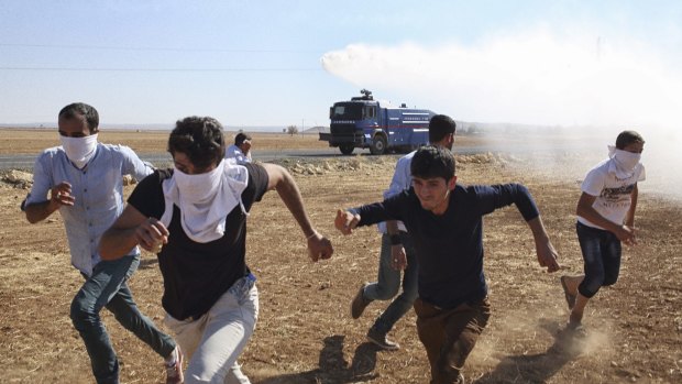 Kurdish protesters on the border near the besieged Syrian town of Kobane flee tear gas fired from a Turkish riot control vehicle on Tuesday.