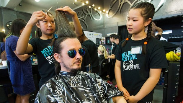 Cing, 12, and Amanda, 12, from Richmond West Primary School cut Cameron Woodhead's hair as part of Melbourne Festival's Haircuts by Children.