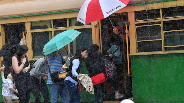 People try to board a tram as rain falls. 