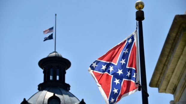 The South Carolina and American flags fly at half-mast behind a Confederate flag flying in front of the State House in Columbia, South Carolina, after Black churchgoers were shot dead last week.
