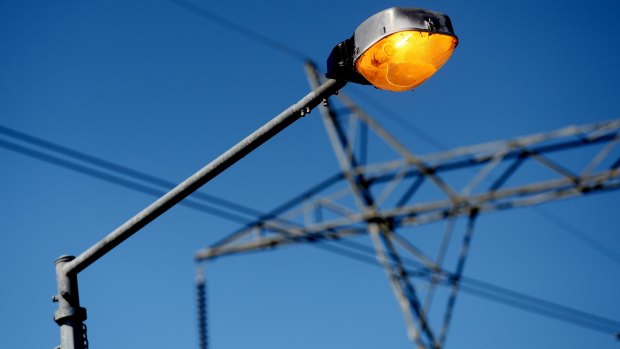 A street light   in front of power lines hanging from an Ausgrid transmission tower in Sydney.